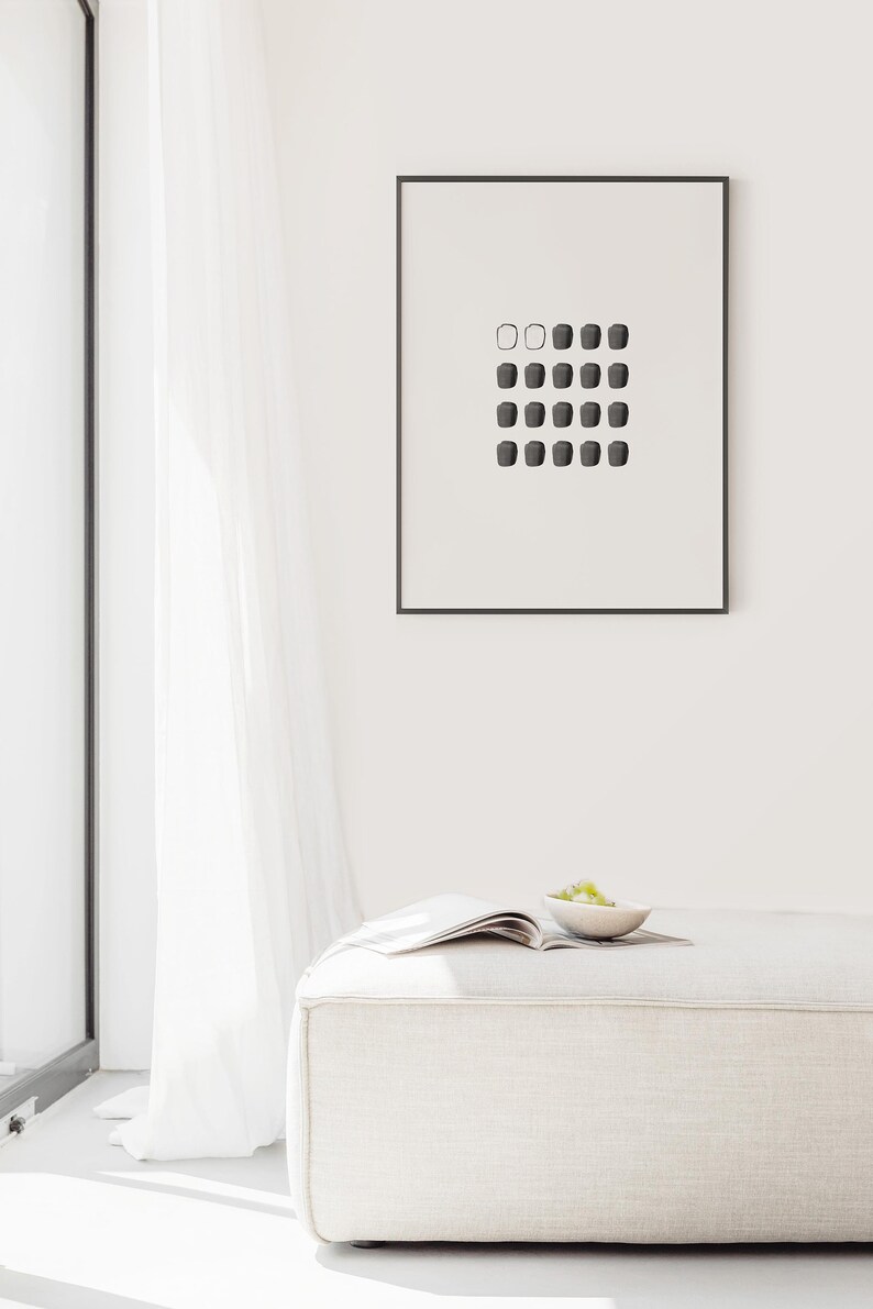 May include: A white, rectangular ottoman with a magazine and a small bowl of green grapes on top. A framed black and white print of a geometric pattern hangs on the wall behind the ottoman.
