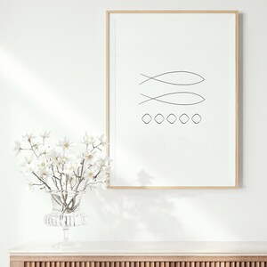 May include: A framed minimalist line art print of two fish symbols and a row of circles on a white background. The print is hanging on a white wall above a wooden cabinet with a white countertop.