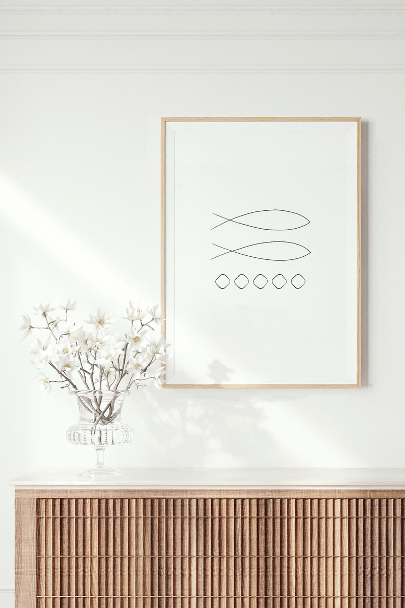 May include: A framed minimalist line art print of two fish symbols and a row of circles on a white background. The print is hanging on a white wall above a wooden cabinet with a white countertop.