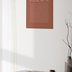 May include: A framed print with a brown background and white text. The text reads "PSALM 91" and includes a passage from the Bible. The print is hanging on a white wall above a wooden table with a vase and dishes.