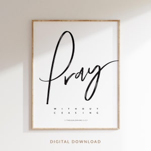 May include: A black and white printable wall art print with the word "Pray" in a handwritten font. The text "Without Ceasing" is below the word "Pray" and the scripture reference "1 Thessalonians 5:17" is below that. The text is on a white background and the print is framed in a light wood frame.