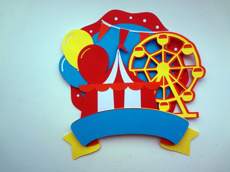 May include: A colorful paper craft set featuring a red and white striped tent, a yellow Ferris wheel, blue and yellow balloons, and a blue banner with a yellow star.