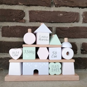 Könnte beinhalten: Ein Satz Holzbausteine in Pastellfarben mit weißen Buchstaben. Die Blöcke buchstabieren "Louisa Mariella", "11.03.2022", "3300g", "50 cm" und "10:34 Uhr".