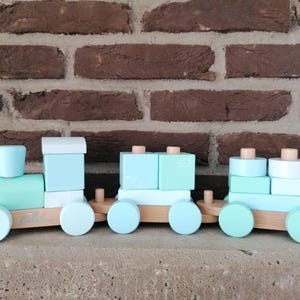 Könnte beinhalten: Ein hellblauer hölzerner Spielzeugzug mit vier Waggons. Jeder Waggon besteht aus gestapelten Blöcken. Der Zug hat Räder und ist für Kinderspiel geeignet.