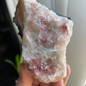 May include: A large, rough, white crystal with pink and green inclusions. The crystal has a natural, raw appearance.