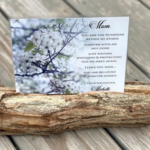 May include: A white card with a black border and a message for a mother. The card is placed on a rustic wooden log. The card reads "Mom. You are the sunshine within my storm. Forever with me not gone. Just waiting watching & protecting till we meet again. I love you mom.... You are so loved & forever missed. Your daughter. Michelle"