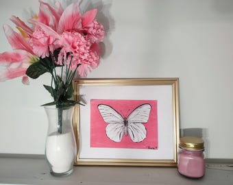 May include: A framed butterfly art print with a gold frame, set against a pink background. A clear vase with pink flowers and a small pink jar with a gold lid are also present, creating a decorative display.