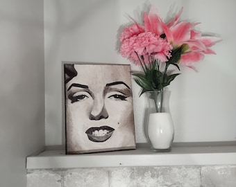 May include: A black and white canvas print of a woman's face with pink flowers in a clear glass vase on a white shelf.