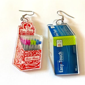 May include: Two pairs of earrings, one with a red and white design featuring the text "Love Roses" and the other with a blue and green design featuring the text "Easy Touch" and "U-100 Insulin Syringes".