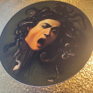 Puede incluir: Un primer plano de una pintura que representa a Medusa, una figura mitol&oacute;gica griega con serpientes por cabello, con una expresi&oacute;n de horror en su rostro.