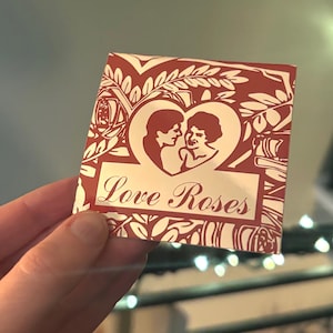 May include: A red and white card with a floral design. The card features a heart with a couple inside and the text "Love Roses".