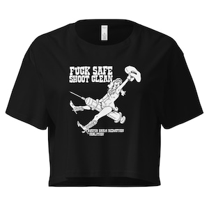 May include: Black crop top t-shirt with a white graphic of a woman riding a syringe, holding a cowboy hat. The text "FUCK SAFE SHOOT CLEAN" is above the graphic, and "AUSTIN HARM REDUCTION COALITION" is below.