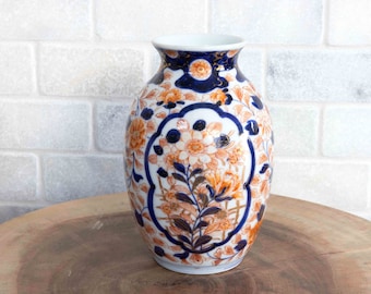 May include: A white porcelain vase with a blue and orange floral pattern. The vase has a round body and a narrow neck.