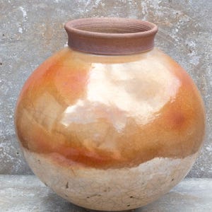 May include: A large, round, ceramic vase with a wide, brown rim. The vase has a light brown glaze with a darker orange glaze on the top half. The glaze has a crackled finish.