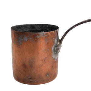 May include: A vintage copper saucepan with a long, dark metal handle. The saucepan has a worn, aged patina.