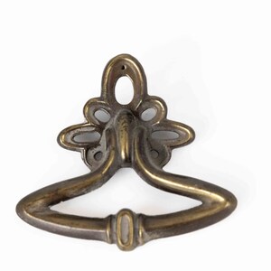 May include: Antique brass drawer pull with a decorative floral design and a curved handle.