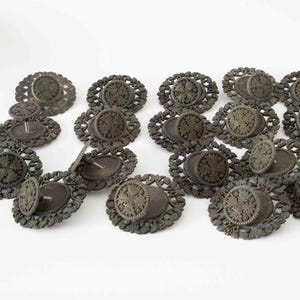 May include: A collection of antique bronze-colored drawer pulls. Each pull features an oval base with a decorative floral design and a circular knob. The knobs are attached to the base with a metal pin.