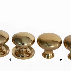May include: Four polished brass cabinet knobs with a round top and a base. The knobs are arranged in a row from left to right. The numbers "1" and "2" are written below the knobs.