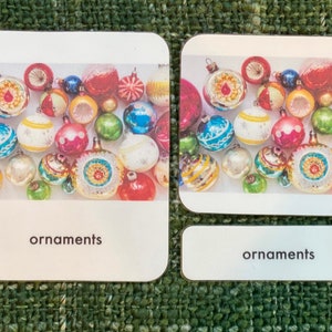 May include: Two cards with a collection of colorful Christmas ornaments. The ornaments are in various shapes and sizes, with a mix of colors including red, blue, green, and gold. The word "ornaments" is printed on the bottom of each card.