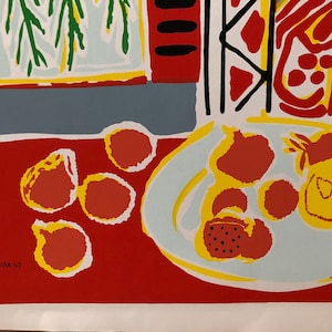 Pu&ograve; includere: Un dipinto di natura morta che presenta un piatto di frutta rossa e gialla su un tavolo rosso. Il piatto &egrave; bianco con un bordo giallo e la frutta &egrave; stilizzata con contorni neri. Lo sfondo &egrave; una parete blu con una pianta verde e gialla.