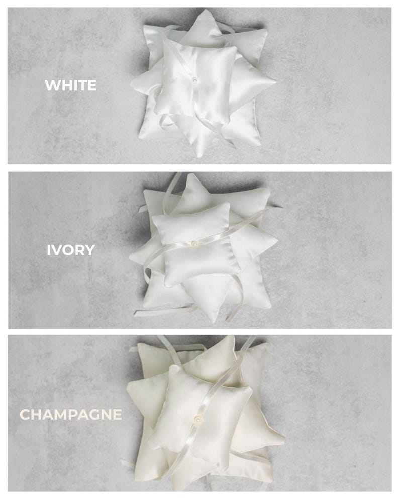 May include: Three ring bearer pillows in white, ivory, and champagne satin. Each pillow is adorned with a ribbon and a pearl. The word "WHITE", "IVORY", and "CHAMPAGNE" are printed above each pillow.
