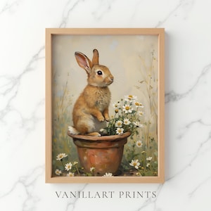 Puede incluir: Una impresión artística enmarcada que muestra un conejo marrón sentado dentro de una maceta de color terracota llena de margaritas blancas. El fondo es un paisaje suave y tenue con hierbas altas y flores blancas adicionales. El texto VANILLART PRINTS es visible en la parte inferior.