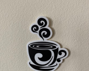 May include: A black and white sticker of a coffee cup with steam rising from the top. The cup has a decorative swirl design on the side and inside the cup. The sticker is on a beige wall.