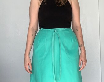 May include: A turquoise green A-line skirt with a tie belt and two pockets. The skirt is knee-length.