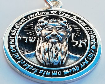 May include: A silver pendant with a detailed image of a bearded man's face. The pendant is inscribed with the words "Ecce faciem et figuram ejus per quem omnia facta sunt et cui omnes obediunt creature" and the Hebrew words "שד" and "אל".