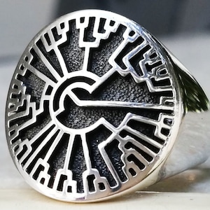May include: A silver ring with a circular design featuring a stylized tree of life pattern. The ring is made of sterling silver and has a polished finish.