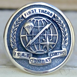 Op de afbeelding: Een zilveren ring met een blauw emaille ontwerp met een wereldbol met een bliksem en een parachute. De ring heeft ook de tekst "First There U.S.A.F. Combat Control" rond de wereldbol.