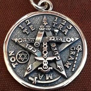 Puede incluir: Un colgante de plata con una estrella de cinco puntas con texto hebreo y símbolos. La estrella está rodeada de un círculo con las palabras "123 Tetragrammaton" inscritas alrededor.
