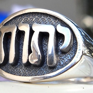 Pode incluir: Um anel de prata com um design oval que apresenta a palavra hebraica "Chai" em letras em relevo.