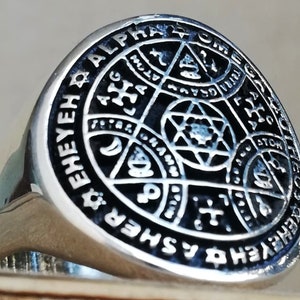Puede incluir: Un anillo de plata con un dise&ntilde;o de esmalte negro que presenta un c&iacute;rculo con las palabras "EHEYEH ALPHA & OMEGA SHEM" alrededor del exterior. El centro del c&iacute;rculo tiene una estrella de David con otros s&iacute;mbolos en su interior.