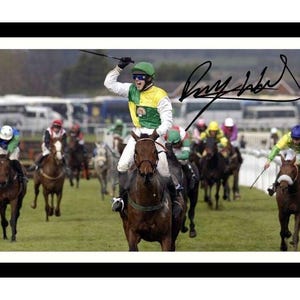 May include: A jockey in a green and yellow racing suit raises his whip in victory as he rides a brown horse across the finish line. Other jockeys and horses are in the background. The signature "Ray Robinson" is visible in the top right corner of the image.