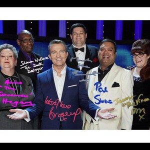May include: A group of six people, including a game show host, stand in front of a blue background. The host is wearing a blue suit and a white shirt. The other people are wearing various outfits. The host is holding a microphone and smiling. The text "Let's have a good time" is written in pink on the image.