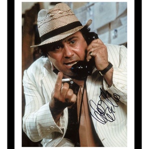 May include: A black and white photograph of a man wearing a white pinstripe suit jacket, a straw hat, and a tie. He is on the phone and holding a cigarette in his other hand. The photo is signed "John Candy".