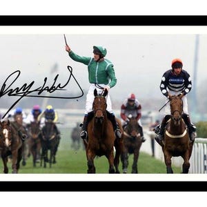 May include: A black and white photograph of a jockey riding a horse in a race. The jockey is wearing a green and white racing suit and a helmet. The horse is brown and has a white star on its forehead. The jockey is holding a whip in his right hand. The photo is signed "Ray Hobbs".