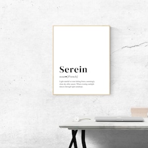 Puede incluir: Un cuadro con la palabra "Serein" en negrita negra. La definición, que describe la lluvia ligera después del atardecer, está debajo. El cuadro está colgado en una pared blanca sobre un escritorio blanco.