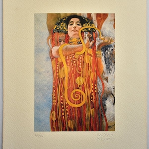 以下が含まれることがあります： グスタフ・クリムトによる「ユディトとホロフェルネス」というタイトルの絵画のプリント。絵画は、赤い金色のローブを着た女性が剣と蛇を持っている様子を描いています。女性の顔は、大きな目と長く細い鼻で、様式化された方法で描かれています。絵画の背景は濃い青で、いくつかの星が見えます。