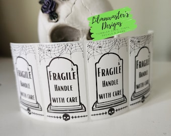 May include: Four white stickers with black text and graphics. The stickers read "Fragile Handle With Care" and feature a skull and crossbones graphic. The stickers are arranged in a row and have a spiderweb design around the edges.