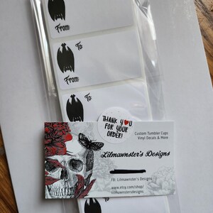 May include: A set of five white gift tags with black bat illustrations and the words "To" and "From". The tags are packaged in a clear plastic bag with a business card that reads "Thank you for your order!" and "Lilmawnster's Designs". The business card also includes the company's social media and website information.