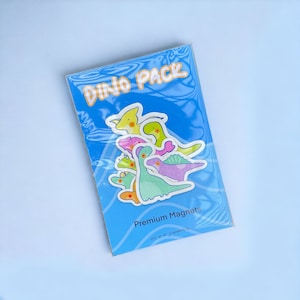 Puede incluir: Un paquete de imanes de dinosaurios coloridos con el texto "Dino Pack" y "Premium Magnets".
