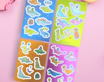 Peut inclure: Quatre feuilles d'autocollants colorés représentant des dinosaures avec des chapeaux de fête et des ballons. Les autocollants sont sur un fond rose.
