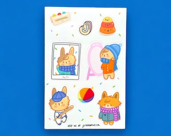 Peut inclure: Une feuille d'autocollants représentant de mignons animaux de dessin animé portant des bonnets d'hiver et jouant au baseball. Les autocollants sont sur un fond blanc avec des confettis colorés. Le texte "visit us at js rainbows.ca" est en bas de la feuille.