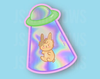 Peut inclure: Un autocollant holographique représentant un lapin de dessin animé en train d'être enlevé par un OVNI. L'OVNI est rose et vert avec une finition holographique.