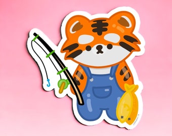 Peut inclure: Autocollant représentant un tigre de dessin animé en salopette bleue, tenant une canne à pêche et un poisson. Le tigre est orange et blanc avec des rayures noires. La canne à pêche est noire et verte, et le poisson est jaune.