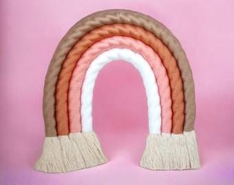 Peut inclure: Une suspension murale en forme d'arc-en-ciel tissé avec un schéma de couleurs brun, orange, rose et blanc. L'arc-en-ciel a une frange en bas.
