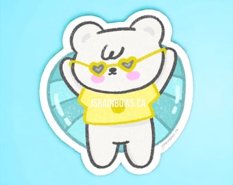 Peut inclure: Un ours blanc portant des lunettes de soleil en forme de cœur et un t-shirt jaune avec le texte "jsrainbows.ca" flotte sur une bouée gonflable bleue et blanche.