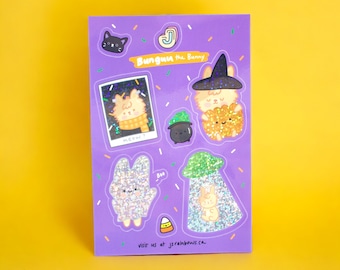 Peut inclure: Un ensemble d'autocollants d'Halloween violets et pailletés représentant un lapin portant un chapeau de sorcière, un chaudron, un lapin dans un cadre photo et un lapin dans un bocal. Le texte "Bunguu the Bunny" et "visit us at jsrainbows.ca" est inclus.